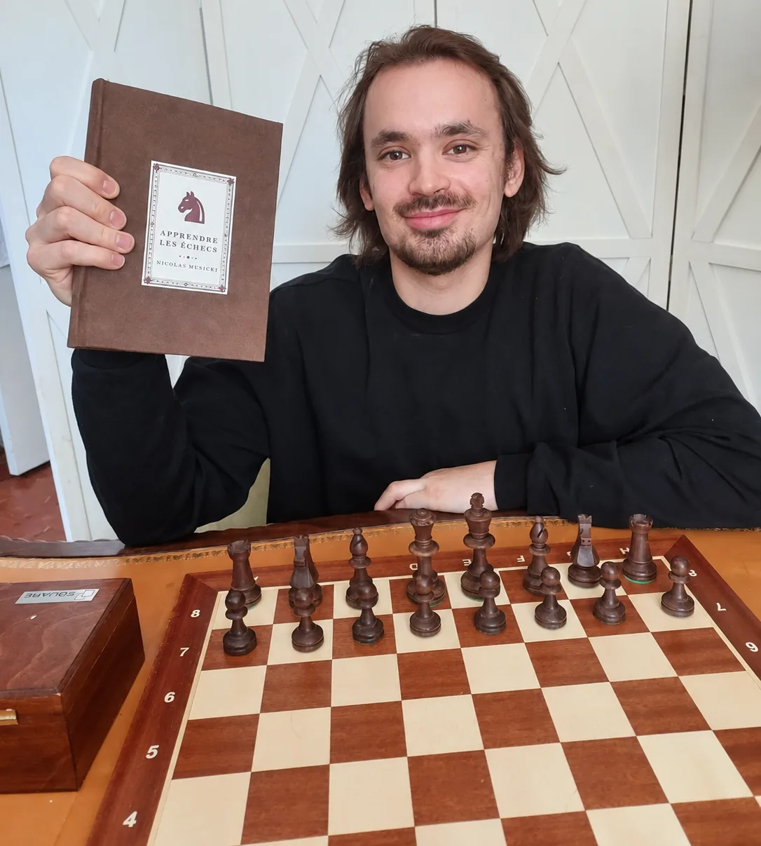 Nicolas Musicki tenant l'édition reliée à la main d'Apprendre les Échecs, 200 pages