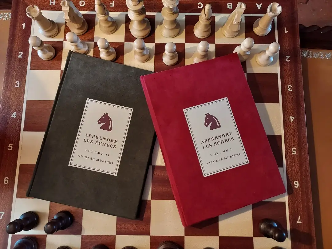 Les deux volumes reliés à la main d'Apprendre les Échecs, posés sur un échiquier en bois